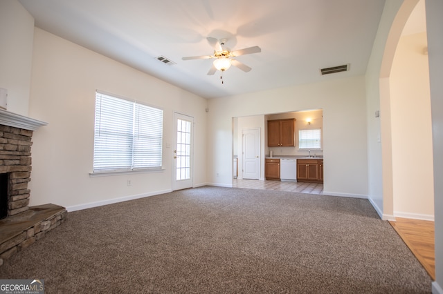 unfurnished living room featuring ceiling fan, a fireplace, sink, and light carpet