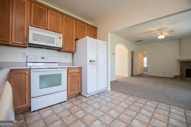 kitchen with ceiling fan, white appliances, a stone fireplace, and light carpet