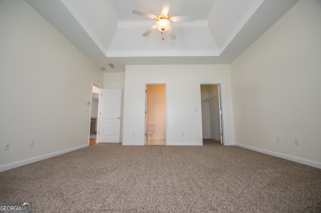 unfurnished bedroom featuring ceiling fan, a tray ceiling, connected bathroom, and carpet floors