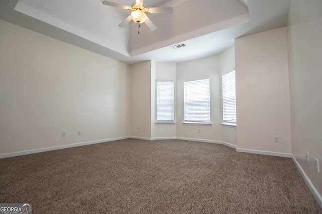 carpeted empty room featuring ceiling fan and a raised ceiling