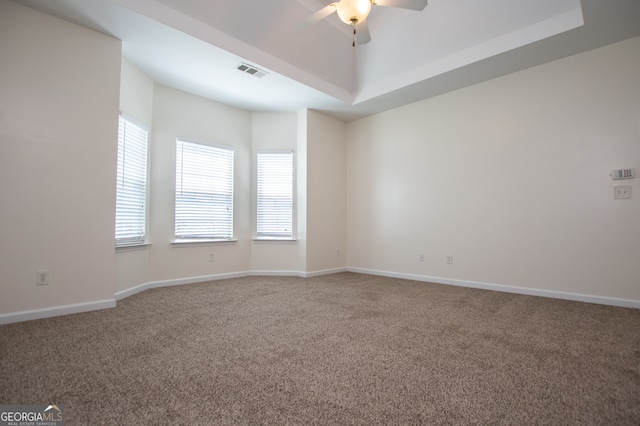 empty room with ceiling fan, a raised ceiling, and carpet