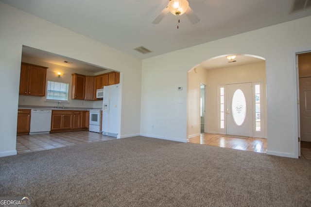 unfurnished living room with ceiling fan, sink, light colored carpet, and plenty of natural light