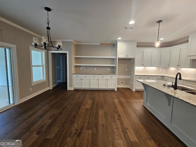 kitchen featuring light stone counters, decorative backsplash, sink, white cabinetry, and a chandelier