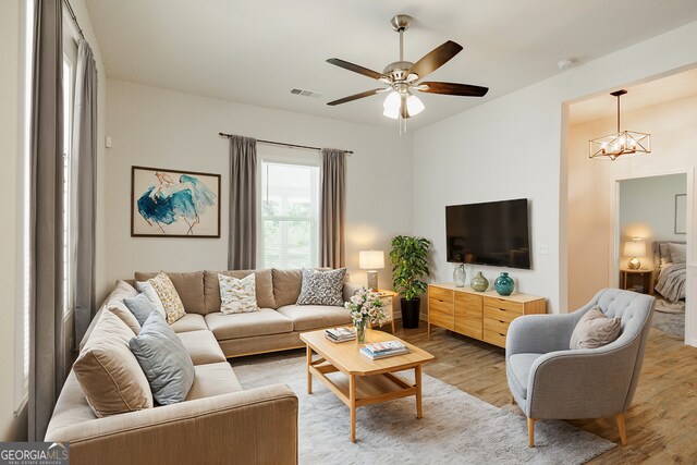 living room featuring ceiling fan with notable chandelier and light wood-type flooring