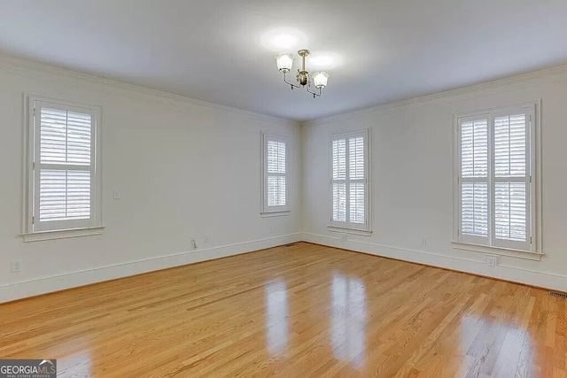 empty room with light hardwood / wood-style flooring, ornamental molding, and an inviting chandelier