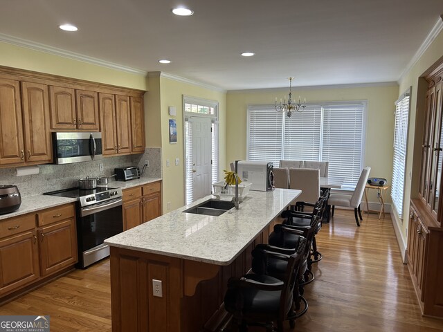 kitchen with appliances with stainless steel finishes, light hardwood / wood-style flooring, tasteful backsplash, a center island with sink, and a wealth of natural light