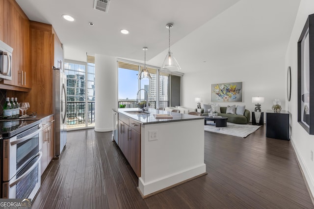 kitchen with floor to ceiling windows, sink, stainless steel appliances, decorative light fixtures, and a center island with sink