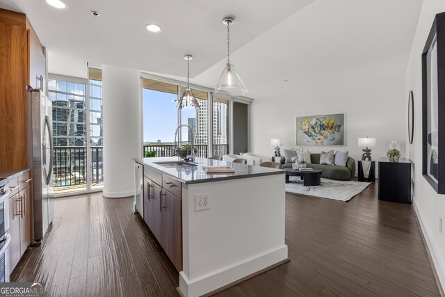 kitchen with floor to ceiling windows, sink, stainless steel appliances, decorative light fixtures, and a center island with sink