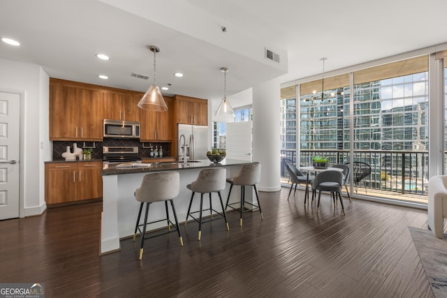 kitchen featuring floor to ceiling windows, hanging light fixtures, stainless steel appliances, a kitchen bar, and a center island with sink