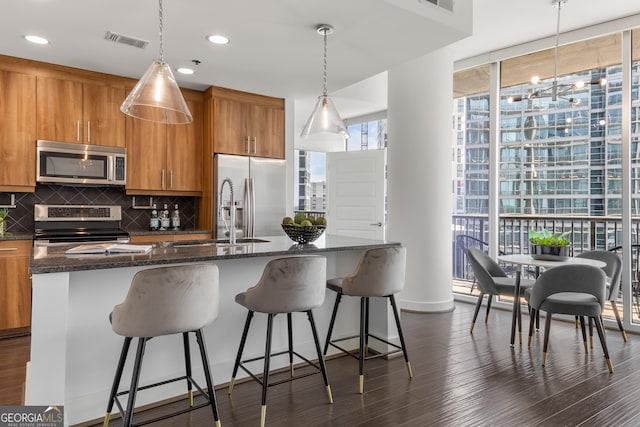 kitchen featuring a kitchen island with sink, hanging light fixtures, appliances with stainless steel finishes, tasteful backsplash, and a wall of windows