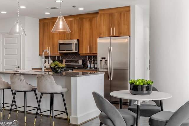 kitchen with backsplash, dark stone counters, a breakfast bar, stainless steel appliances, and decorative light fixtures