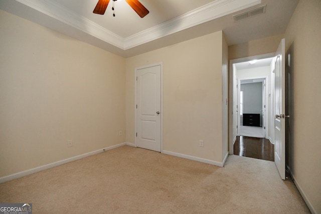 unfurnished bedroom featuring ceiling fan, light carpet, crown molding, and a tray ceiling