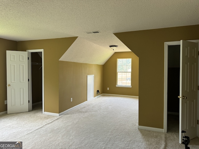 additional living space featuring vaulted ceiling, a textured ceiling, and carpet