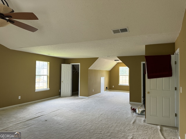 additional living space featuring ceiling fan, lofted ceiling, light carpet, and a textured ceiling