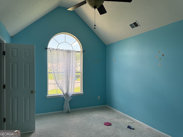 carpeted spare room featuring ceiling fan, lofted ceiling, a textured ceiling, and a wealth of natural light