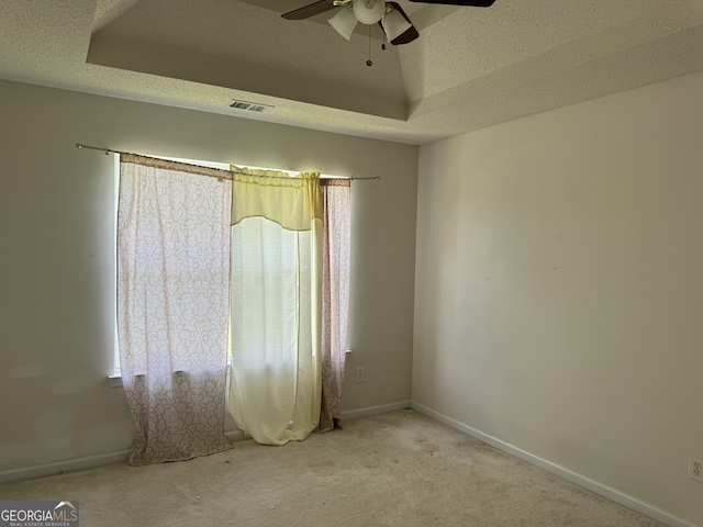 carpeted empty room with ceiling fan, a raised ceiling, and a textured ceiling