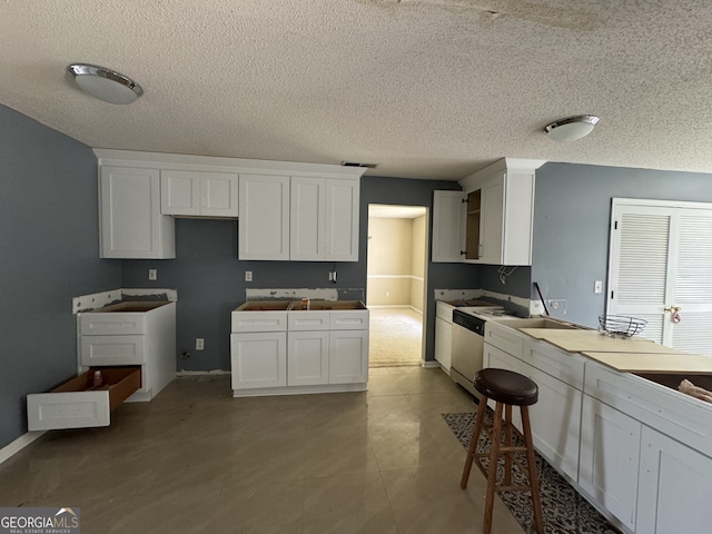 kitchen featuring white cabinetry, stainless steel dishwasher, light tile patterned flooring, and a textured ceiling