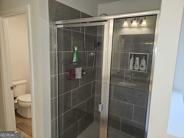 bathroom with a shower with door, hardwood / wood-style flooring, and toilet