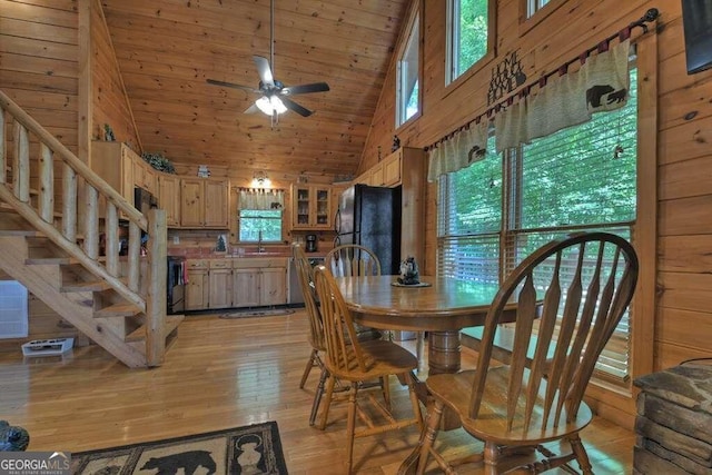 dining space featuring ceiling fan, light wood-type flooring, high vaulted ceiling, sink, and wood walls