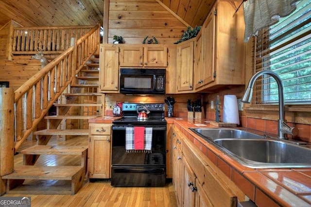 kitchen with lofted ceiling, wood walls, light hardwood / wood-style floors, black appliances, and sink