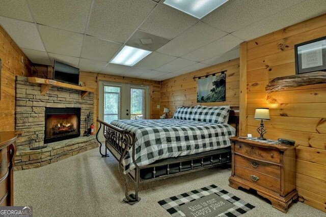 bedroom featuring a fireplace, wood walls, carpet, and a drop ceiling