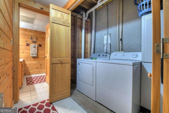 laundry area featuring light tile patterned flooring, washing machine and clothes dryer, and wooden walls