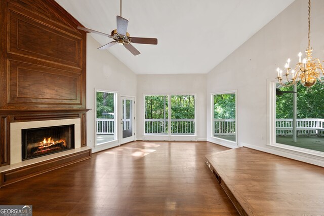 unfurnished living room with ceiling fan with notable chandelier, hardwood / wood-style flooring, and high vaulted ceiling