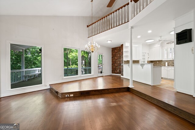 unfurnished living room with wood-type flooring, ceiling fan with notable chandelier, and high vaulted ceiling