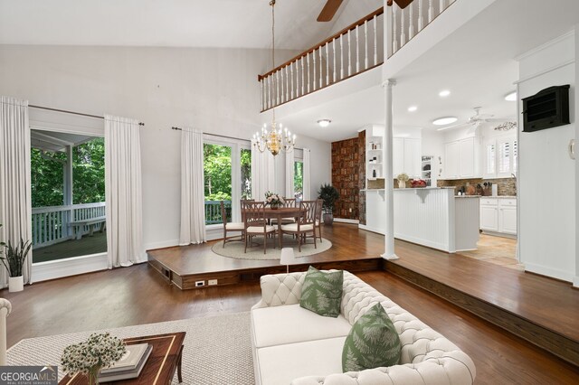 living room with ceiling fan with notable chandelier, hardwood / wood-style floors, and high vaulted ceiling