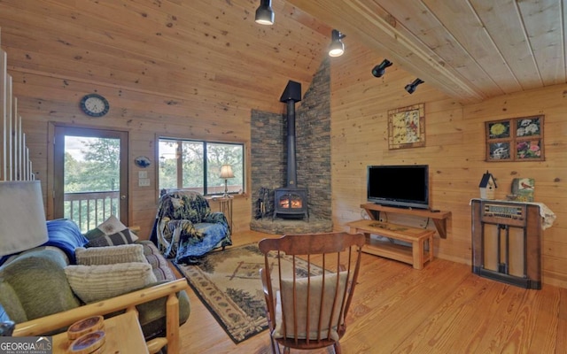 living room featuring light wood-type flooring, a wood stove, wooden ceiling, and wood walls