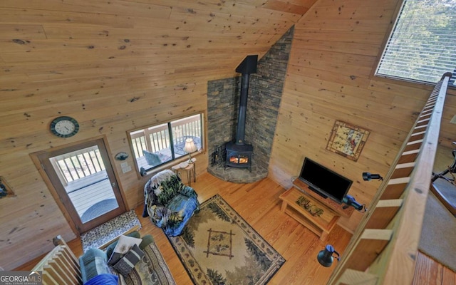 living room with hardwood / wood-style floors, a wood stove, high vaulted ceiling, and wooden walls