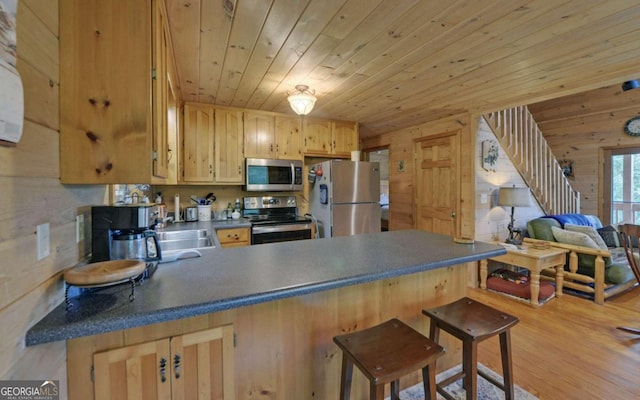 kitchen with stainless steel appliances, light wood-type flooring, a breakfast bar area, wood walls, and kitchen peninsula