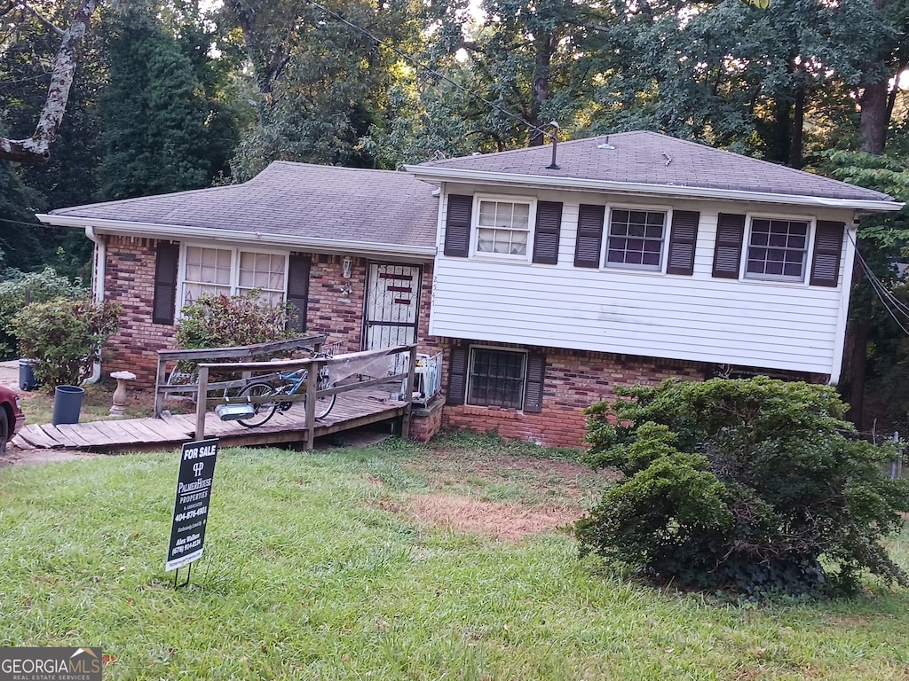 tri-level home featuring a wooden deck and a front yard