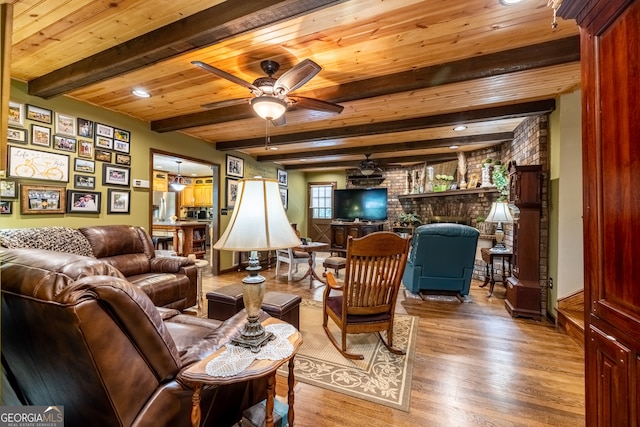 living room featuring beamed ceiling, hardwood / wood-style floors, a brick fireplace, brick wall, and ceiling fan