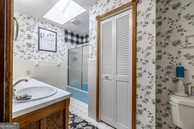 bathroom featuring a skylight, toilet, vanity, tile walls, and tile patterned floors