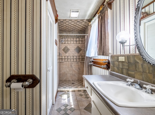 bathroom featuring tiled shower, vanity, tile patterned floors, tile walls, and a textured ceiling