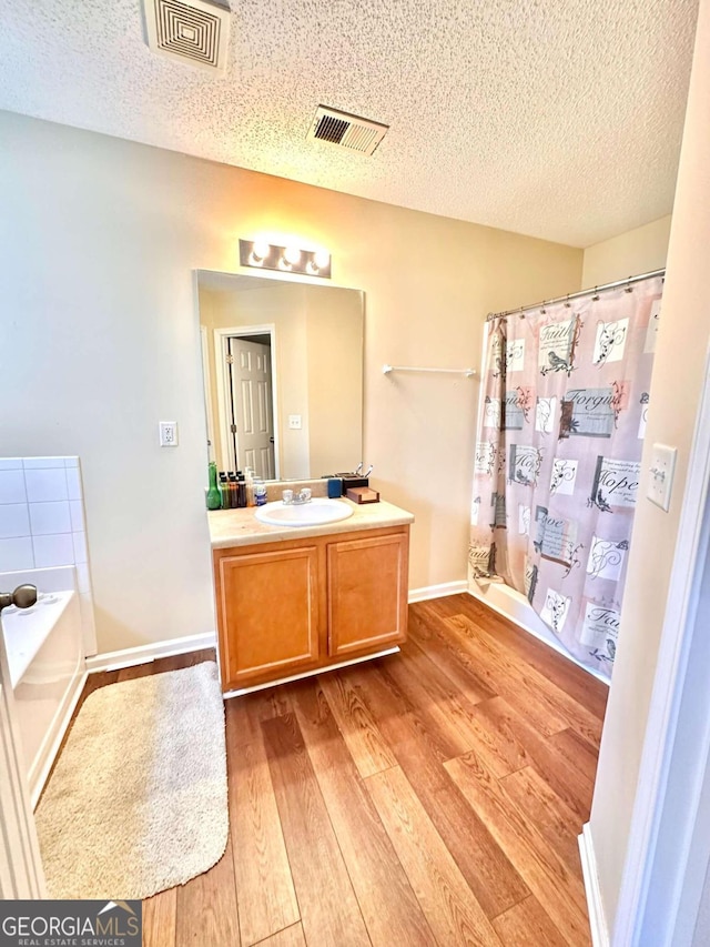 bathroom with vanity, a textured ceiling, a tub to relax in, and hardwood / wood-style floors