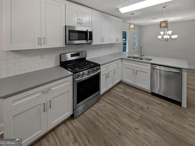 kitchen featuring appliances with stainless steel finishes, kitchen peninsula, light hardwood / wood-style flooring, and decorative light fixtures