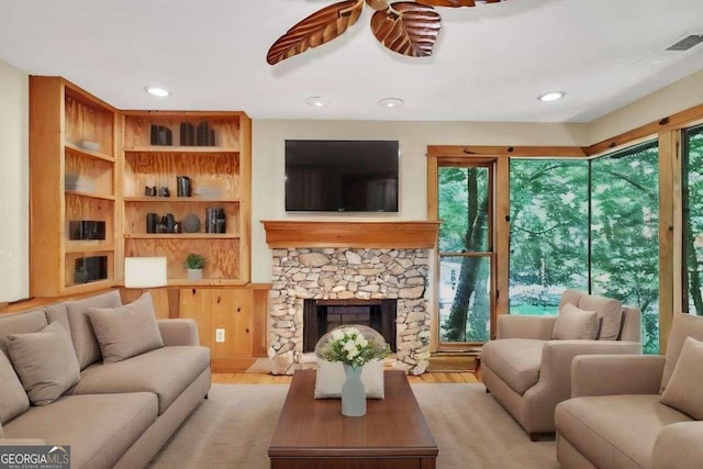 living room featuring built in features, a fireplace, ceiling fan, and light wood-type flooring