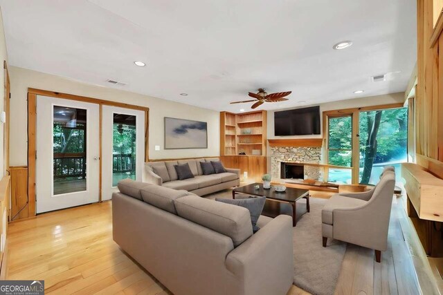 living room with plenty of natural light, a fireplace, light wood-type flooring, and built in shelves