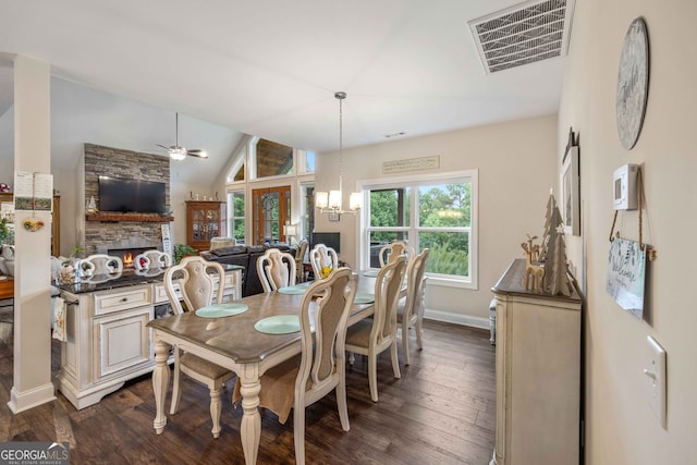 dining room with a stone fireplace, ceiling fan with notable chandelier, dark hardwood / wood-style flooring, and vaulted ceiling