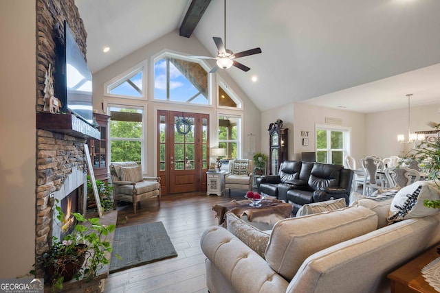 living room with beamed ceiling, hardwood / wood-style floors, a stone fireplace, ceiling fan with notable chandelier, and high vaulted ceiling