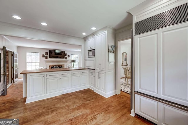 kitchen with built in microwave, white cabinets, kitchen peninsula, crown molding, and light hardwood / wood-style flooring