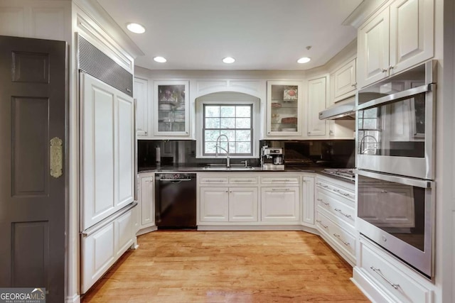 kitchen with sink, white cabinetry, light wood-type flooring, appliances with stainless steel finishes, and decorative backsplash