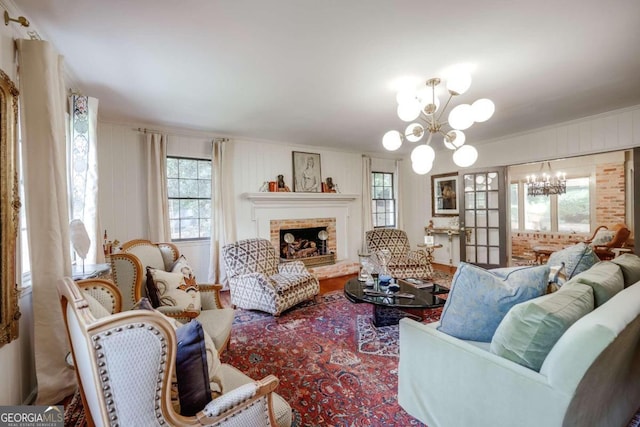 living room featuring ornamental molding, a brick fireplace, a healthy amount of sunlight, and a chandelier