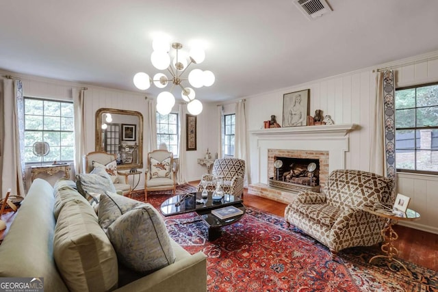 living room with a brick fireplace, wood-type flooring, ornamental molding, and a chandelier