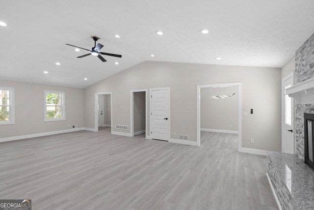 unfurnished living room featuring ceiling fan, light hardwood / wood-style floors, a stone fireplace, and lofted ceiling