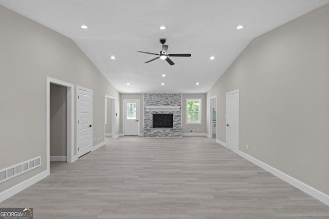 unfurnished living room featuring light hardwood / wood-style floors, vaulted ceiling, a stone fireplace, and ceiling fan