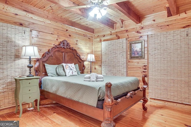 bedroom featuring wood walls, beamed ceiling, wood-type flooring, ceiling fan, and wooden ceiling