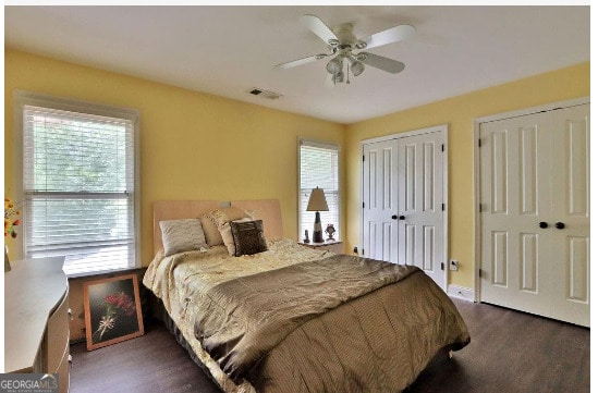 bedroom with multiple closets, dark hardwood / wood-style floors, multiple windows, and ceiling fan